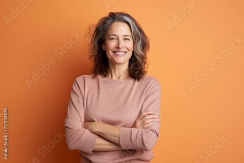 Portrait of smiling middle aged woman with crossed arms on orange background