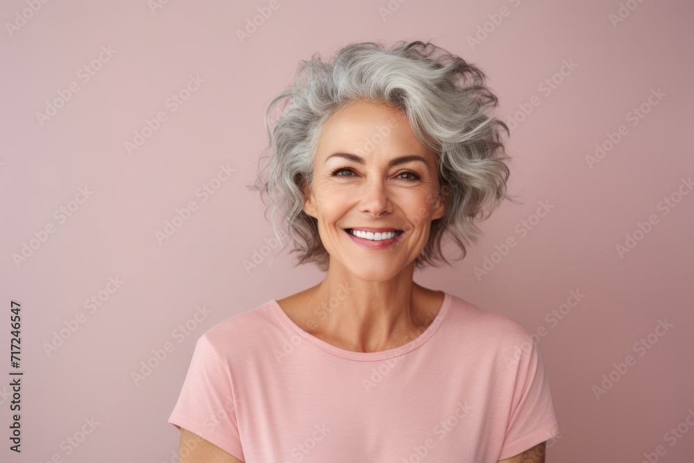 Portrait of smiling senior woman with grey hair on pink background.