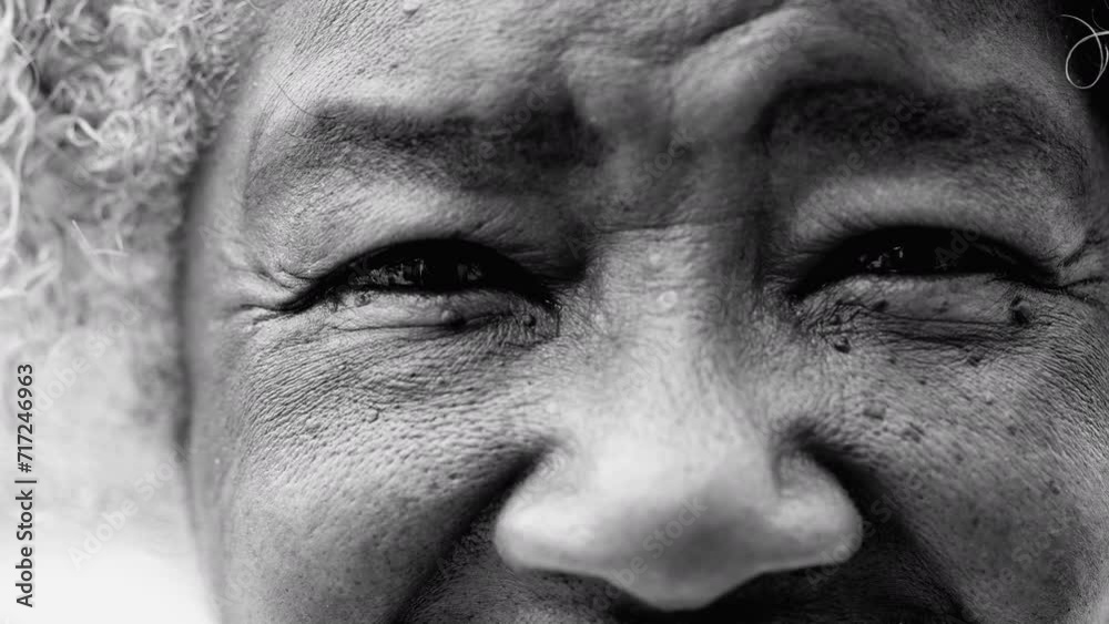 Macro closeup of a wrinkled black senior woman eyes looking at camera depicting old age and wisdom in black and white. African American detail face