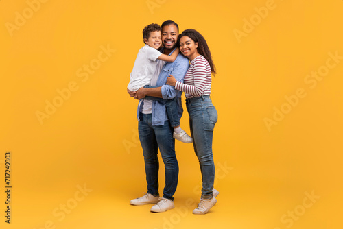 Happy Young Black Parents With Their Little Son Posing On Yellow Background © Prostock-studio