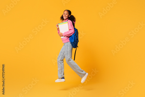 Happy black student girl jumping with backpack and workbooks, studio
