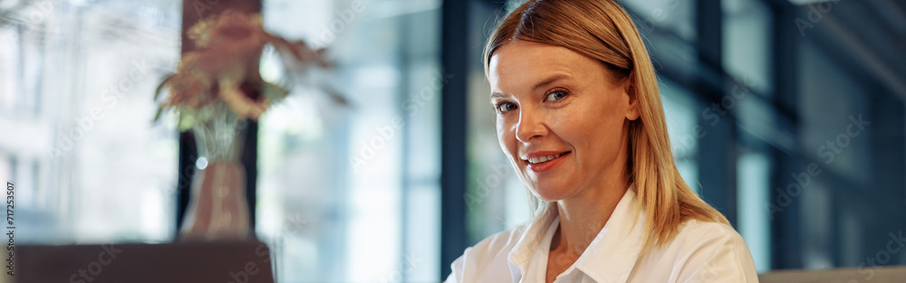 Woman entrepreneur working on laptop while sitting in cozy coworking and looking at camera Woman entrepreneur working on laptop while sitting in cozy coworking and looking at camera
