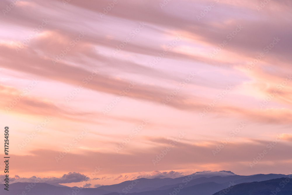 A beautiful serene lilac sunset overlooking layers of hills and mountains, sweeping clouds and soft warm light. A picture that is quite meditative and peaceful that could be used to promote wellbeing