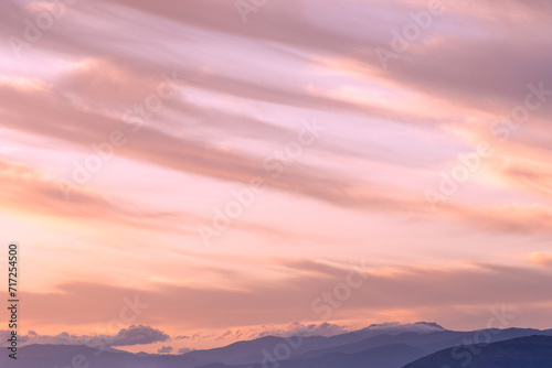 A beautiful serene lilac sunset overlooking layers of hills and mountains, sweeping clouds and soft warm light. A picture that is quite meditative and peaceful that could be used to promote wellbeing © andrew