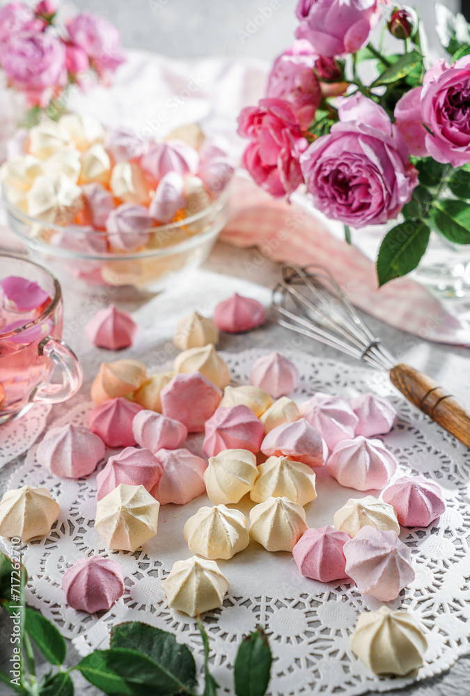Pastel coloured meringues, zephyr, on lace napkin with cup of tea and rose flowers on light background. Sweets, dessert and pastry, homemade cakes, top view, selective focus