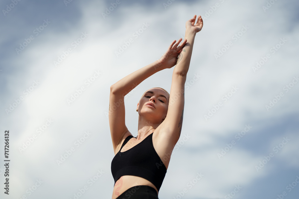 A woman engages in a calming stretching exercise, reaching towards the sky in a fitness routine A woman engages in a calming stretching exercise, reaching towards the sky in a fitness routine