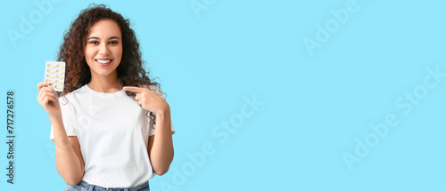 Young African-American holding fish oil pills on light blue background with space for text photo
