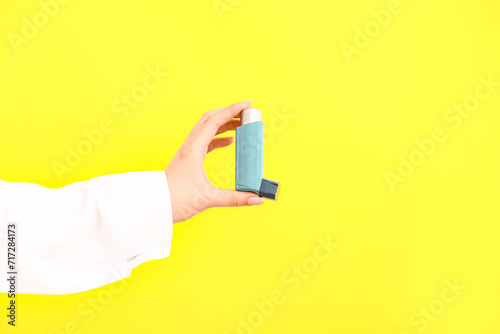 Female doctor hand with inhaler on yellow background