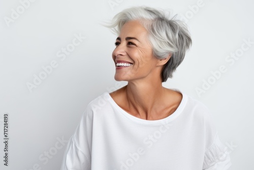 Portrait of a happy senior woman smiling and looking away while standing against grey background