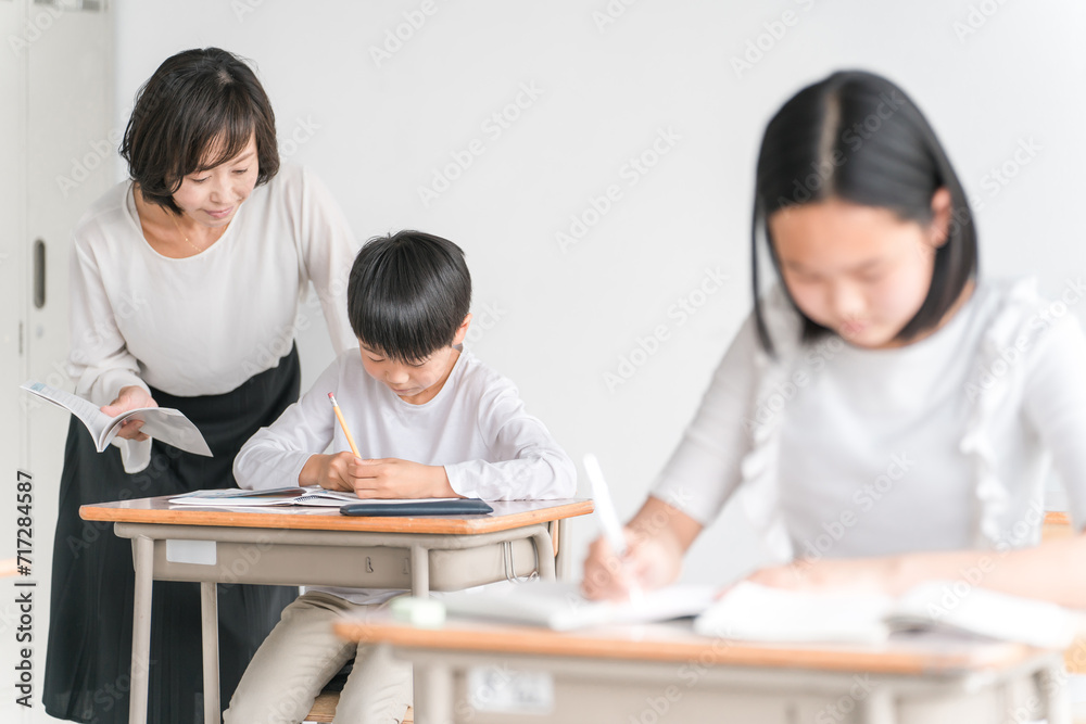 学校の教室・塾で先生と話す高学年のアジア人男子生徒（学童・児童クラブ・学童保育・学習・教育）
