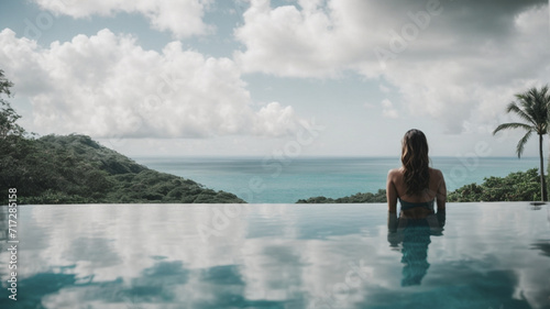 panoramic image Rear view of a woman relaxing serenely in an infinity pool, contemplating a stunning tropical view, embodying tranquility and natural beauty. 