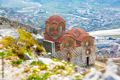 View of Byzantine style building of medieval Holy Trinity Church on green flowering slope of hill in Berat in rays of spring sun, Albania