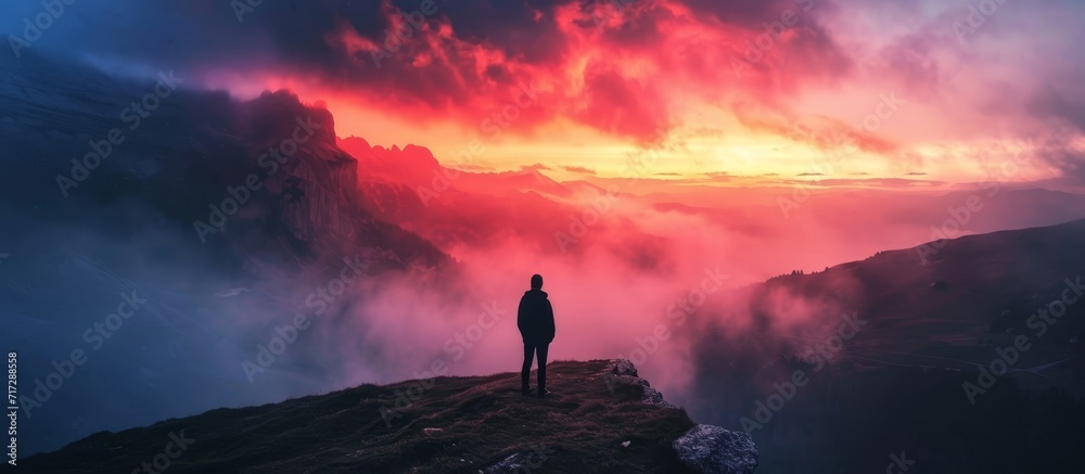Man witnessing a colorful autumn sunset at Dolomites Landscape, surrounded by foggy hills and a beautiful dusk sky in the Alps. - obrazy, fototapety, plakaty 