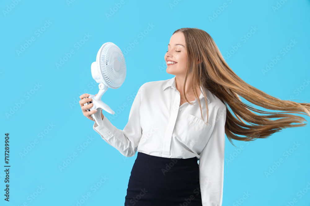 Young businesswoman with electric fan on blue background Young businesswoman with electric fan on blue background