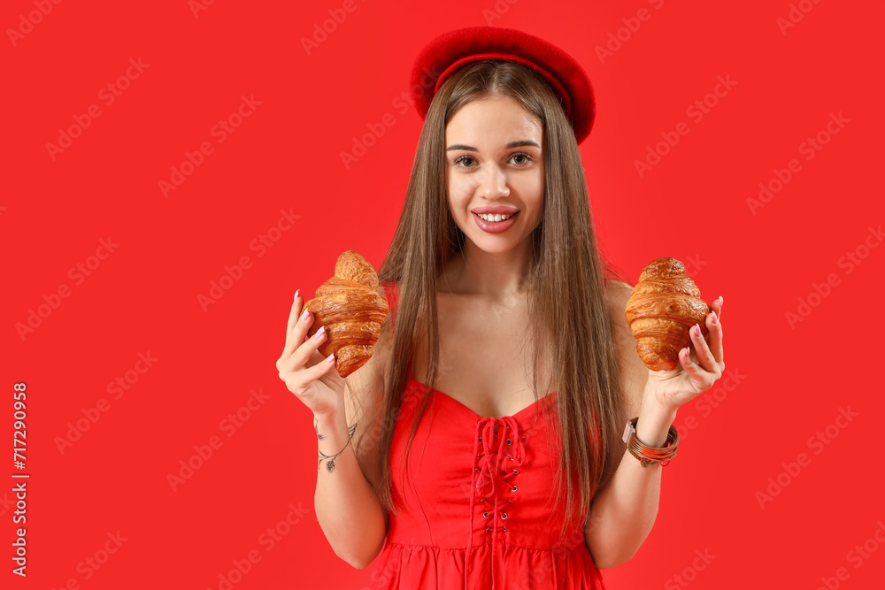Beautiful young woman in beret with tasty croissants on red background Beautiful young woman in beret with tasty croissants on red background