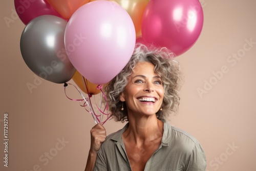 Portrait of a happy senior woman holding balloons, looking up and smiling © Igor