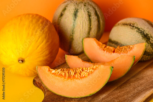 Wooden board with tasty ripe melons on orange background