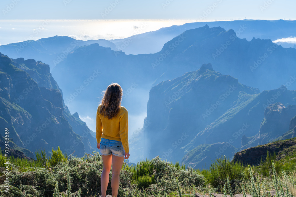 Obraz premium Female tourist enjoys picturesque view from the summit of a volcanic island on a sunny summer day. Pico do Arieiro, Madeira Island, Portugal, Europe.