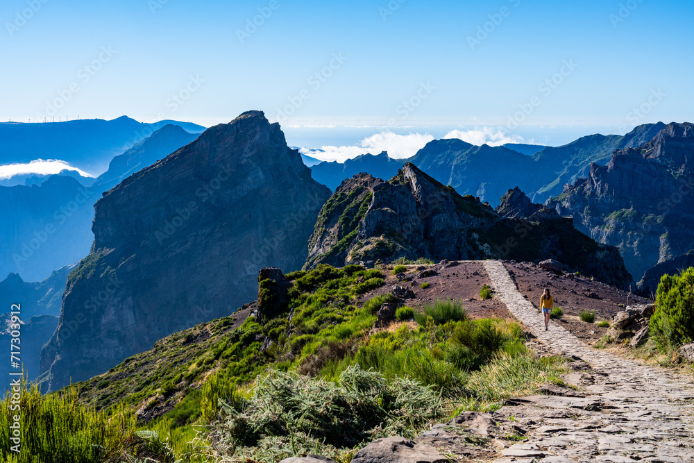 Naklejka premium Female tourist walks along panoramic mountain trail and enjoys the picturesque view on a sunny summer day. Pico do Arieiro, Madeira Island, Portugal, Europe.