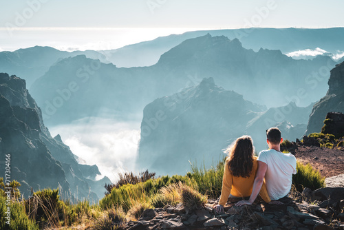 Tourist couple enjoys the panoramicview from the mountain top of a volcanic island on a sunny summer day. Pico do Arieiro, Madeira Island, Portugal, Europe.
