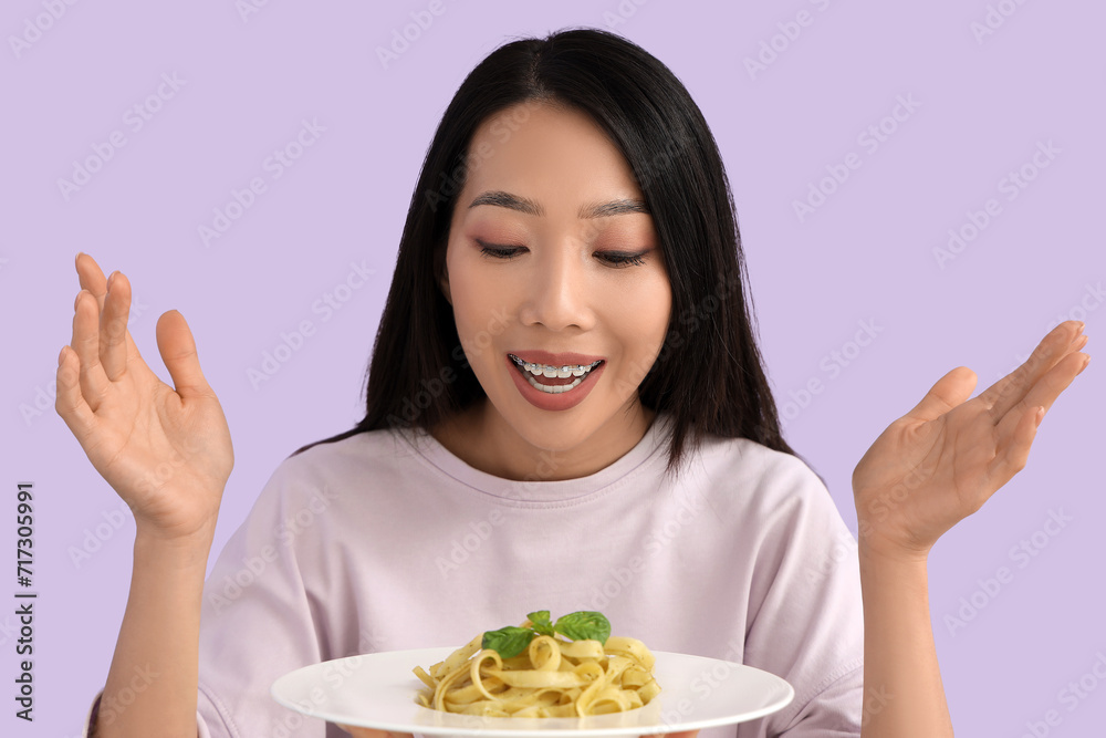 Young Asian woman with tasty pasta on lilac background, closeup Young Asian woman with tasty pasta on lilac background, closeup
