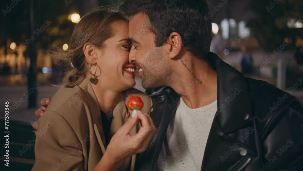 Playful couple enjoying date kissing night closeup. Smiling pair with strawberry