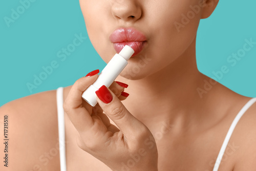 Young woman applying lip balm on color background  closeup