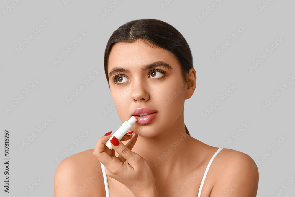 Beautiful young woman applying lip balm on grey background Beautiful young woman applying lip balm on grey background