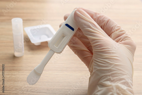 Woman holding disposable express test above wooden table, closeup