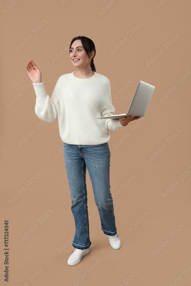 Pretty young woman with laptop on beige background