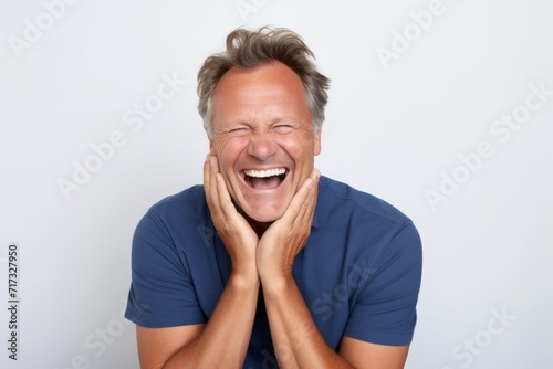 Portrait of happy senior man laughing and looking at camera against grey background © Iigo