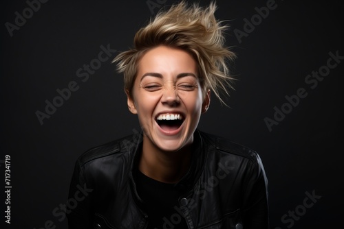 Portrait of a happy young woman in black leather jacket screaming on black background © Iigo