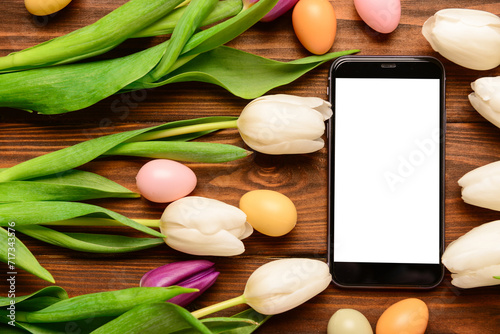 Composition with modern mobile phone, beautiful tulip flowers and Easter eggs on wooden background