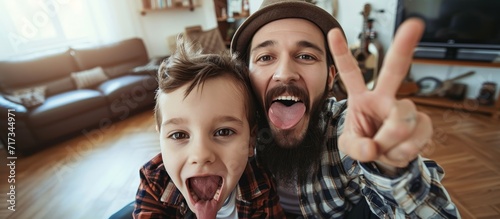 Happy father and son taking a selfie indoors, making punk symbols and sticking out their tongues. photo