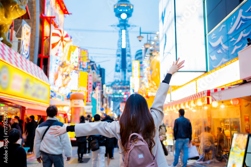 Asian female tourist Traveling and having fun. And she was taking photo with a cell phone camera at Night street with many restaurant around Tsutenkaku Tower in Shinsekai district of Osaka, Japan.