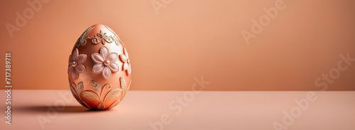 Golden egg with flower decorations on a peach colored banner background with copy space. Easter concept