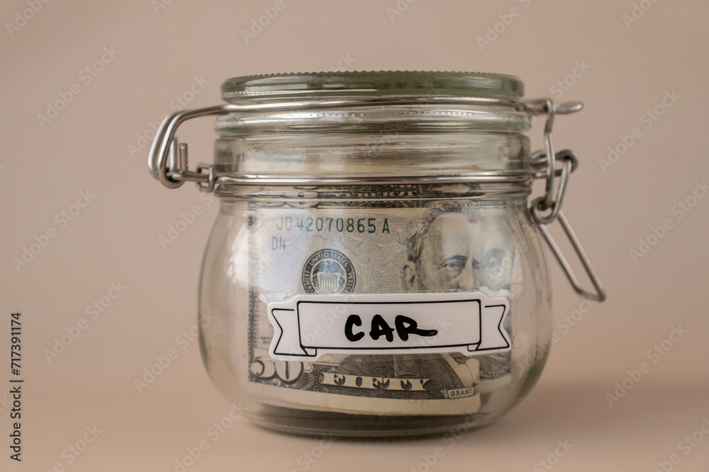 Glass jar full of American currency dollars cash banknote with text CAR. Preparation saving money. Moderate consumption and economy Glass jar full of American currency dollars cash banknote with text CAR. Preparation saving money. Moderate consumption and economy