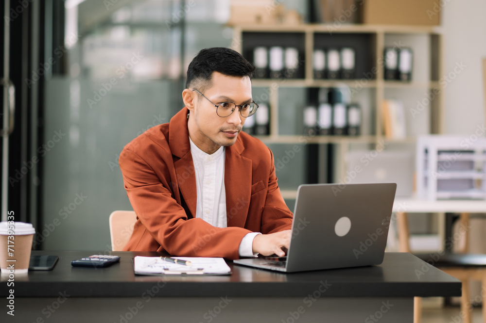Young attractive man using laptop and tablet while sitting at her working place. Concentrated at work. Young attractive man using laptop and tablet while sitting at her working place. Concentrated at work.