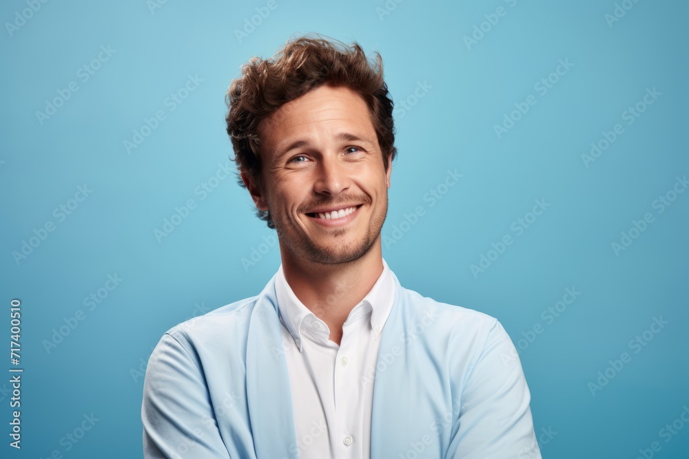 Handsome young man looking at camera and smiling while standing against blue background Handsome young man looking at camera and smiling while standing against blue background