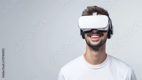 Portrait of young man wearing virtual reality glasses over white background with copy space. Smiling man in white VR goggles. photo