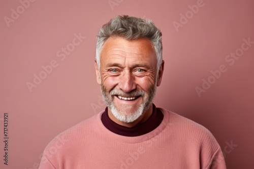 Portrait of a smiling senior man looking at the camera over pink background. © Inigo