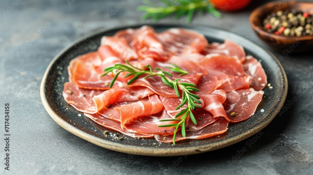 Thinly sliced prosciutto garnished with fresh rosemary on a dark plate Thinly sliced prosciutto garnished with fresh rosemary on a dark plate