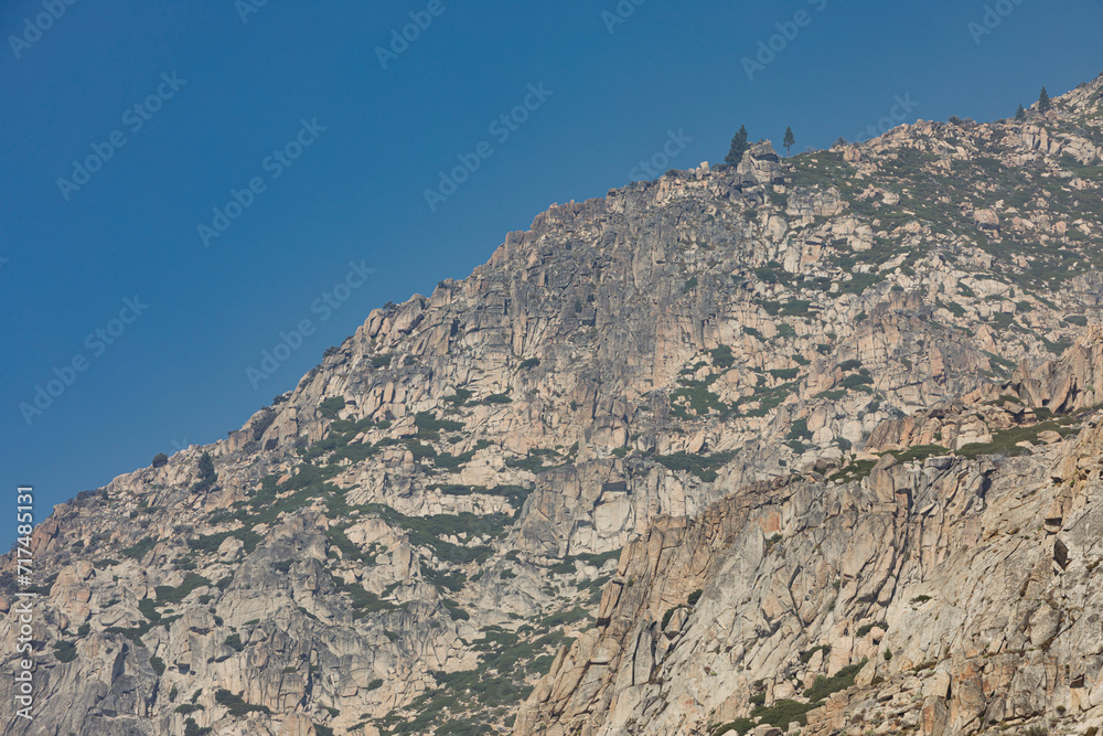 A very rocky mountain with a few trees and green patches in California against a blue sky on a Sunny Summer day. Nr.1