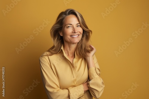 Smiling mature woman with hand on hip isolated on yellow background.