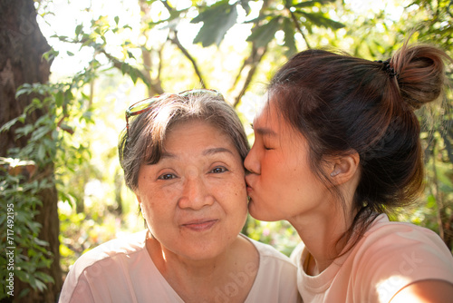 Close up of Happy asian Thai Chinese daughter kissing her elder mother cheek, while relaxing sitting and drinking at cafe in garden. © Suthida