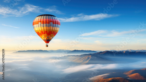 Scenic view of a colorful hot air balloon soaring above foggy mountain peaks during a serene sunrise.