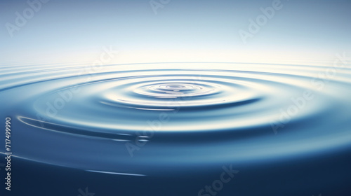 A single water droplet creating a ripple effect on the tranquil surface of clear blue water. © red_orange_stock