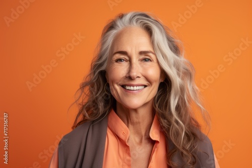 Happy senior woman. Portrait of beautiful mature woman looking at camera and smiling while standing against orange background © Iigo