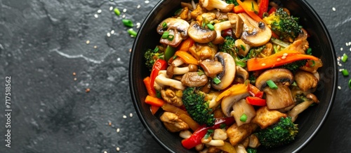 Close-up view of a plant-based stir fry with mushrooms and veggies in a black bowl, against a slate background.