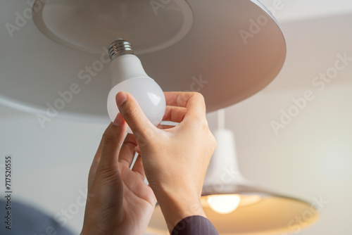 Cropped image of woman hands changing light bulb in hanging lamp at home.